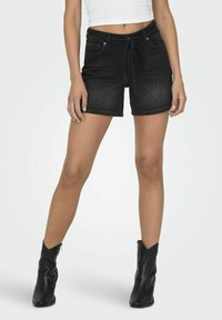 Shorts en denim noir avec taille à cordon de serrage, poches avant et coupe slim. Assortis à des bottes en cuir noir jusqu'à la cheville.