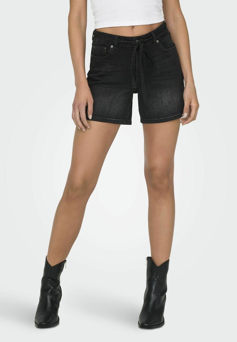Shorts en denim noir avec taille à cordon de serrage, poches avant et coupe slim. Assortis à des bottes en cuir noir jusqu'à la cheville.