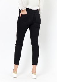 Jeans ajustados negros de tiro alto con dobladillo deshilachado, que cuentan con bolsillos traseros estándar y un acabado elegante, combinados con zapatillas blancas.