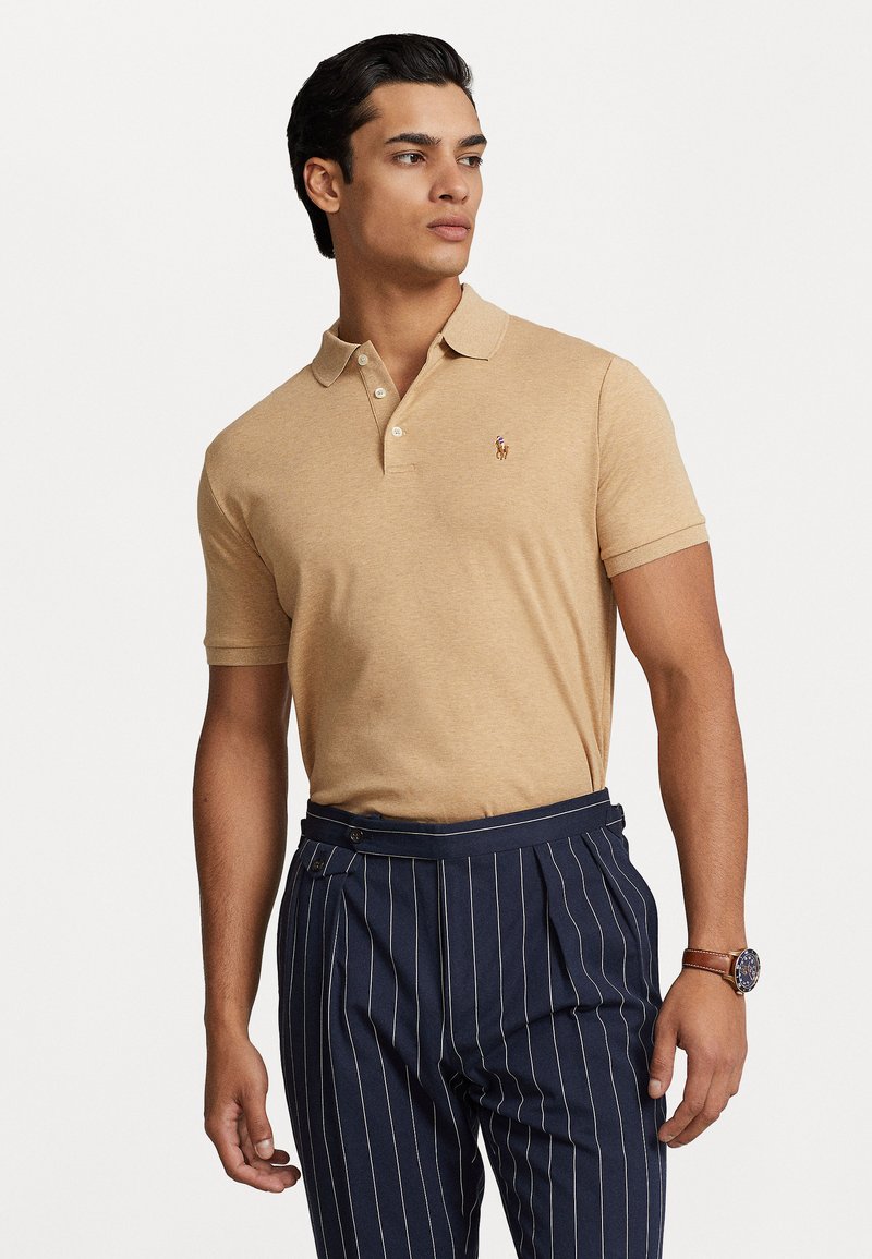 Karamelli polo särk kolme nupuga kaeluses ja tikitud logoga. Koos navy siniste triibuliste pükste jaheduses. Sile kanga tekstuur ja lõigetüüp.
