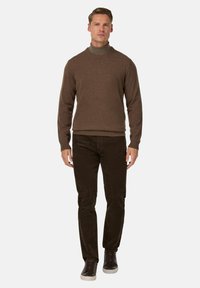 Brązowy sweter dzianinowy z wysokim kołnierzem, w zestawieniu z ciemnobrązowymi spodniami sztruksowymi i ciemnymi sneakersami. Prosty design o miękkiej teksturze.