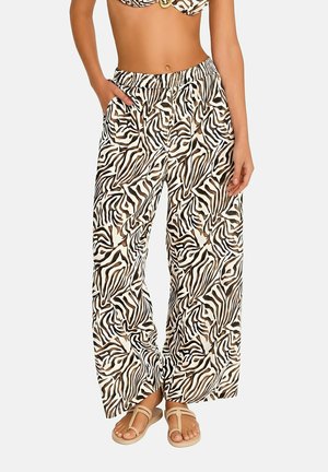 Femme portant un pantalon à jambes larges avec imprimé zèbre et un haut de bikini assorti, debout les mains dans les poches avec des sandales beiges.