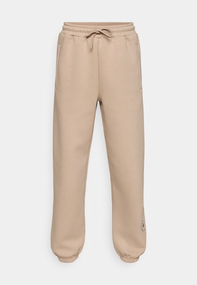 Μπεζ φόρμες με ελαστική μέση και κορδόνι, με πλαϊνές τσέπες και ριμπ μανσέτες στον αστράγαλο. Διακριτική λεπτομέρεια με μινιμαλιστικό λογότυπο στο μηρό.