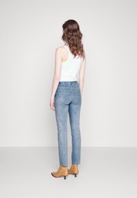 Jeans de denim de color azul claro con corte ajustado, dobladillo sin terminar y diseño de cinco bolsillos, combinados con botas de tobillo de color beige. Camiseta de tirantes blanca lisa.