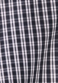 Tissu à carreaux noir et blanc avec des rayures verticales et horizontales de tailles variées formant un motif à carreaux.