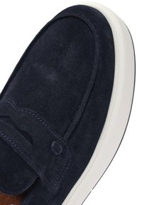 Zapato de ante azul marino con diseño slip-on, suela de goma blanca y detalles de costura a lo largo del collar y la parte delantera.