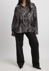 Blusa nera a maniche lunghe con un motivo ondulato crema e beige, realizzata in tessuto morbido, abbinata a pantaloni neri a gamba larga e tacchi a punta.