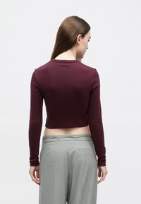 Bordo pikkade varrukatega lühike särk ümmarguse kaelusega, kombineeritud helehallide kõrge vöökohaga pükstega, stiilitud siledaks viimistluseks.