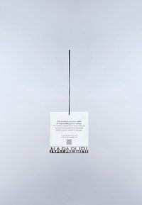 Een rechthoekig wit label met een zwart ophangkoord, waarop een label staat met de tekst "NAPAPIJRI" in vetgedrukt. Tekst met details over verantwoord katoen gebruik.