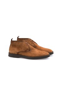 Bottines en suède marron avec une texture lisse, un bout rond et un design de laçage minimal. Comprend une semelle en caoutchouc noir et une languette au talon.