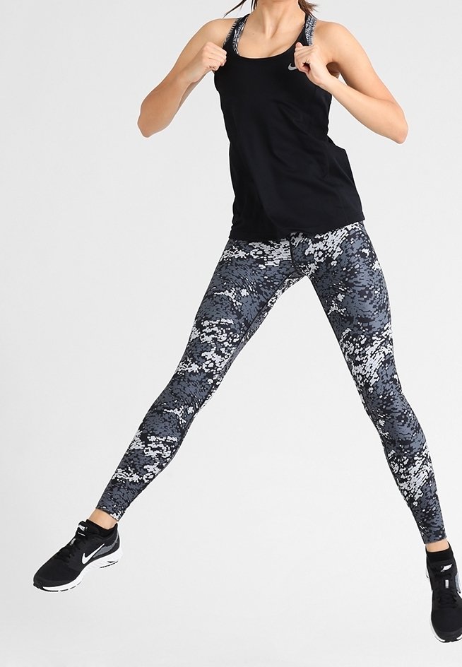 Zwarte sportieve tanktop gecombineerd met grijze camouflagelegging met witte accenten en een gestructureerd patroon; zwarte sneakers maken de outfit compleet.
