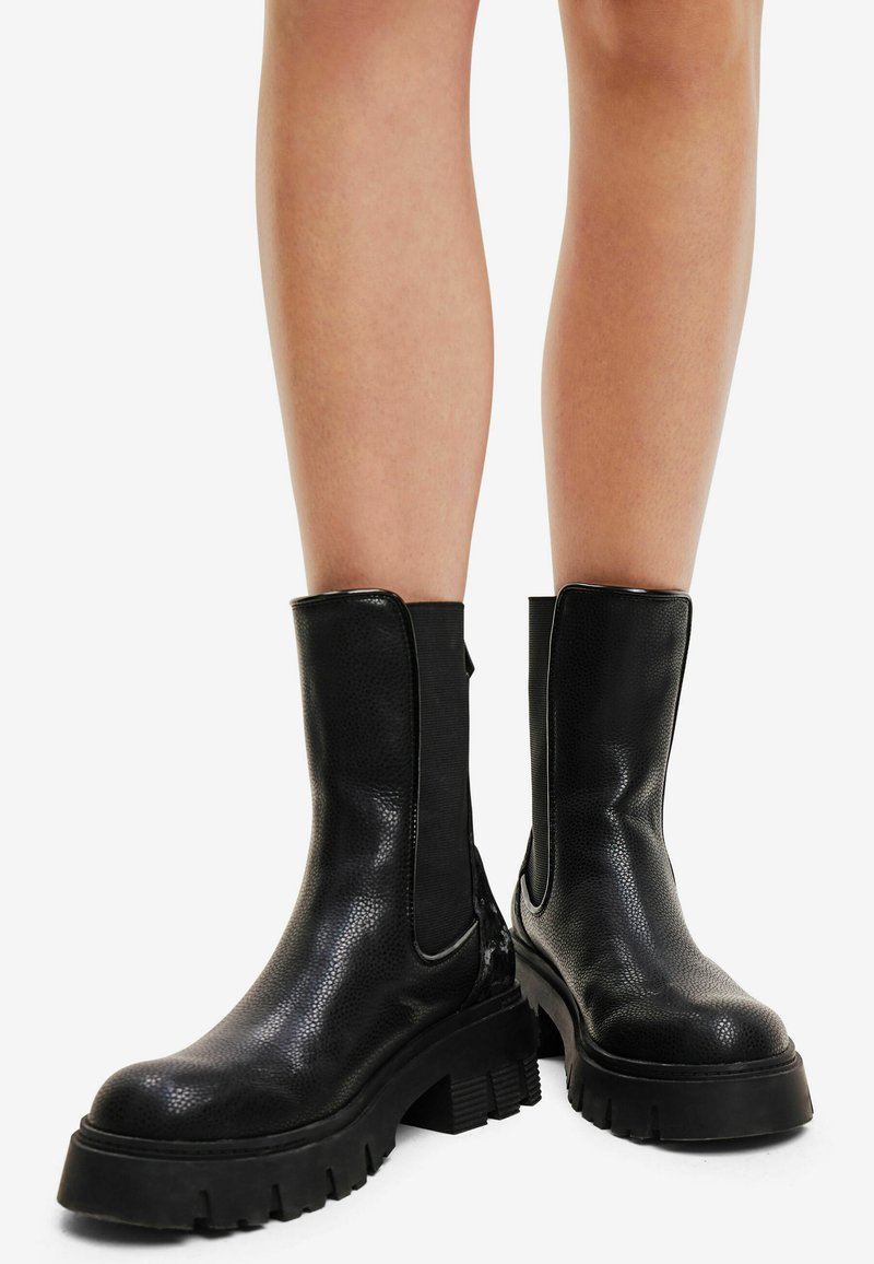 Stivali neri alla caviglia con finitura in pelle testurizzata, pannelli elastici ai lati e suole in gomma spessa, dotati di punta arrotondata e tacco basso.