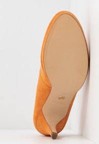 Talons hauts en daim orange avec un bout pointu et une semelle beige lisse. Présente un subtil accent doré près du talon.