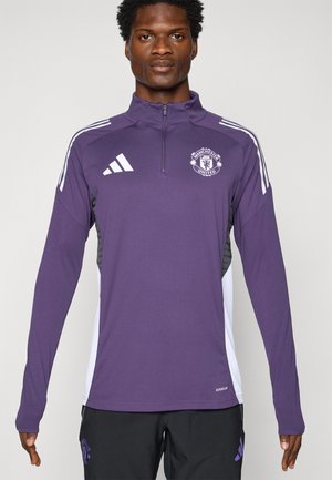 Lilla atletisk jakke med lynlås krave, der har hvide skulderstriber og Manchester United-logo. Fremstillet af glat, let materiale.