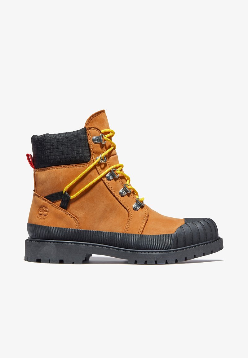 Botte de travail en cuir marron avec col rembourré noir, lacets jaunes, embout renforcé en caoutchouc noir et semelle noire épaisse à rainures.