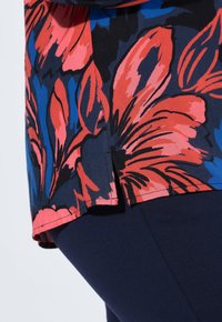 Maglietta a maniche corte con motivo floreale in rosso e blu su sfondo nero. L'orlo presenta spacco laterale e una texture di tessuto liscia.