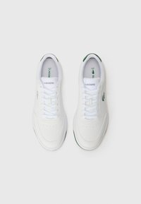 Witte sneakers met een glad bovenwerk van synthetisch materiaal, veters en geperforeerde details. Groene accenten op de hiel en het logo. Rubberen zool.