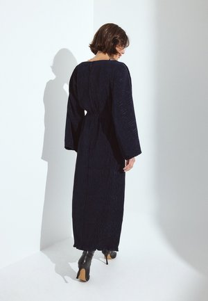 Abito lungo navy in tessuto texturizzato, con maniche ampie e vita strizzata, abbinato a stivali neri con tacco a martello.