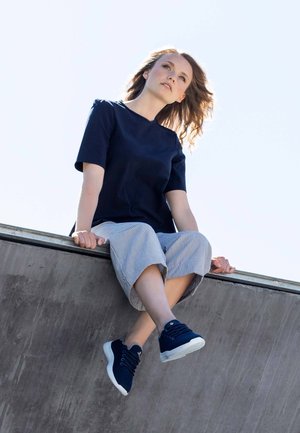 Navy short-sleeve top, striped cropped pants, and navy sneakers. Smooth fabric, relaxed fit, and distinct button detailing on the top.
