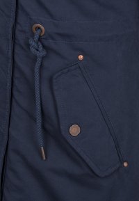 Chaqueta azul marino con tejido texturizado, cuerda trenzada y acentos de hardware en tono cobre en el bolsillo frontal y el cierre.