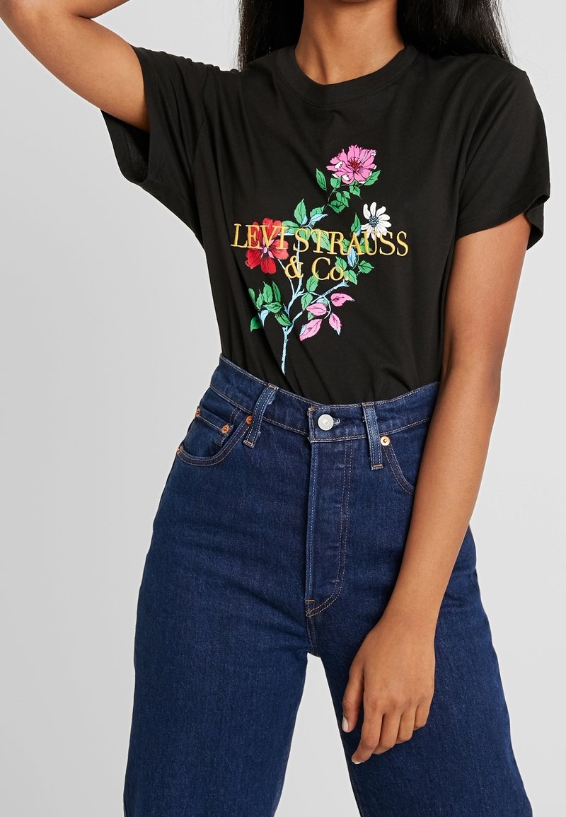 Czarna koszulka bawełniana z kolorową haftowaną florystyką oraz złotym napisem „LEVI STRAUSS & CO”. W parze z wysokogatunkowymi niebieskimi dżinsami.