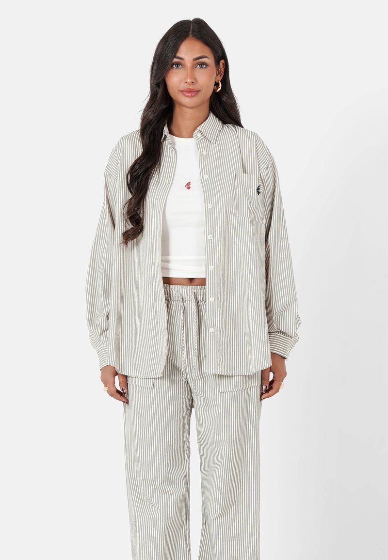 Hvid- og gråstribet button-up skjorte parret med matchende loose-fit bukser; har en brystlomme og afslappede ærmer. Glat stoftekstur.