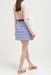 Maglia rosa chiaro a maniche lunghe abbinata a una gonna a righe blu e bianche. La gonna presenta pieghe e una fascia in vita aderente. Completano il look delle ballerine color bronzo.