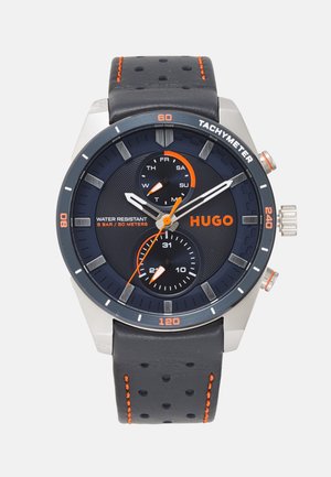 Analoge horloge met roestvrijstalen kast, zwarte wijzerplaat, zilveren indexen en oranje accenten. Geperforeerde zwarte leren band. Waterbestendig, chronograaf functies.