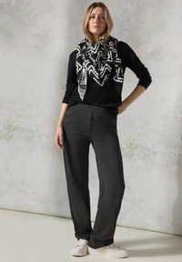 Maglione nero a maglia abbinato a pantaloni larghi grigio scuro e una sciarpa a zigzag bianco e nero. Il modello indossa sneaker bianche.
