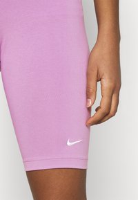 Vaaleanpunaiset Nike-shortsit, joissa on sileä ja joustava kangas. Shortseissa on valkoinen logo alas myyjän kohdalla, ne ovat istuvat ja ulottuvat keskimmäiseen reiteen.
