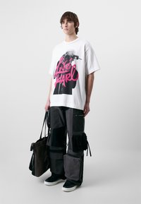 Witte oversized t-shirt met grafische print; zwart, grijs patchwork cargobroek met meerdere zakken; zwarte sneakers; totebag.