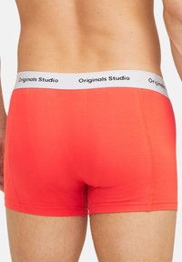 Un boxer rouge en tissu doux avec une ceinture élastique blanche portant l'inscription "Originals Studio" en noir.