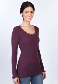 Langärmliges, lila, geripptes Oberteil mit einem gewellten Spitzen-Ausschnitt und Rüschensaum. Figurbetontes Design, glatte Textur, leichtes Material.