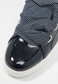 Baskets en cuir verni bleu marine avec un superposé en tissu texturé à rayures. Bout rond, semelle en caoutchouc blanche et lacets avec œillets.