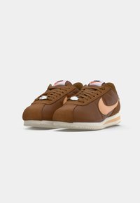 Smeđe kožne tenisice s antilop detaljima i bež gumeno potplat. Imaju breskvast Nike logotip i bijele vezice.