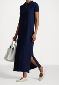 Námořnická modrá polo šaty s krátkým rukávem, bočním rozparkem, vyrobené z bavlny. Vybaveno s bílou kabelkou a světlou obuví.