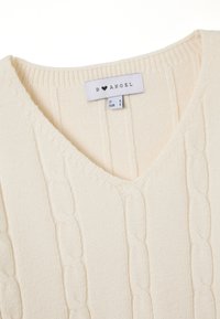 Cremfarbener Strickpullover mit V-Ausschnitt, strukturiertem Zopfmuster und geripptem Ausschnitt. Das Etikett weist auf die Größe S und die Marke "B ♥ ANGEL" hin.
