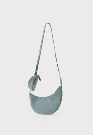 Lyseblå ruskind skuldertaske i halvmåneform med justerbar rem og lille rundt lynlåslomme fastgjort.