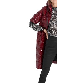 Bordeaux pufferjack met een glanzende afwerking, geheven ontwerp en capuchon, over een grijs luipaardprint top en zwarte broek.