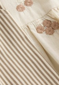 Beige fabric with embroidered brown flowers and cream and brown narrow vertical stripes, showing texture and gathered stitching details.