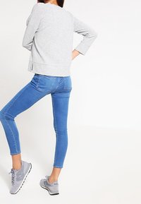 Grauer gestreifter Pullover mit abgerundetem Saum, kombiniert mit blauen Skinny-Jeans und grauen Sportschuhen. Sichtbare Seitennahtakzente.
