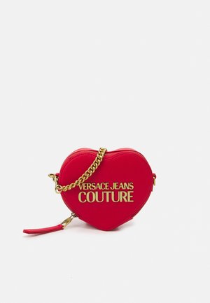 Sac rouge en forme de cœur avec une chaîne dorée et le texte « Versace Jeans Couture » en lettres dorées à l’avant.