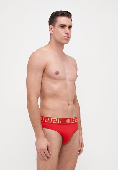 Rote Schwimmslips mit einem goldenen griechischen Schlüssel-Muster am Bund. Glattes, elastisches Material mit einem tiefgeschnittenen Design.