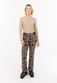 Beige zip-nekt langemouwen top gecombineerd met patroon slim-fit broeken in beige en bruine tinten, aangevuld met zwarte skibotten.