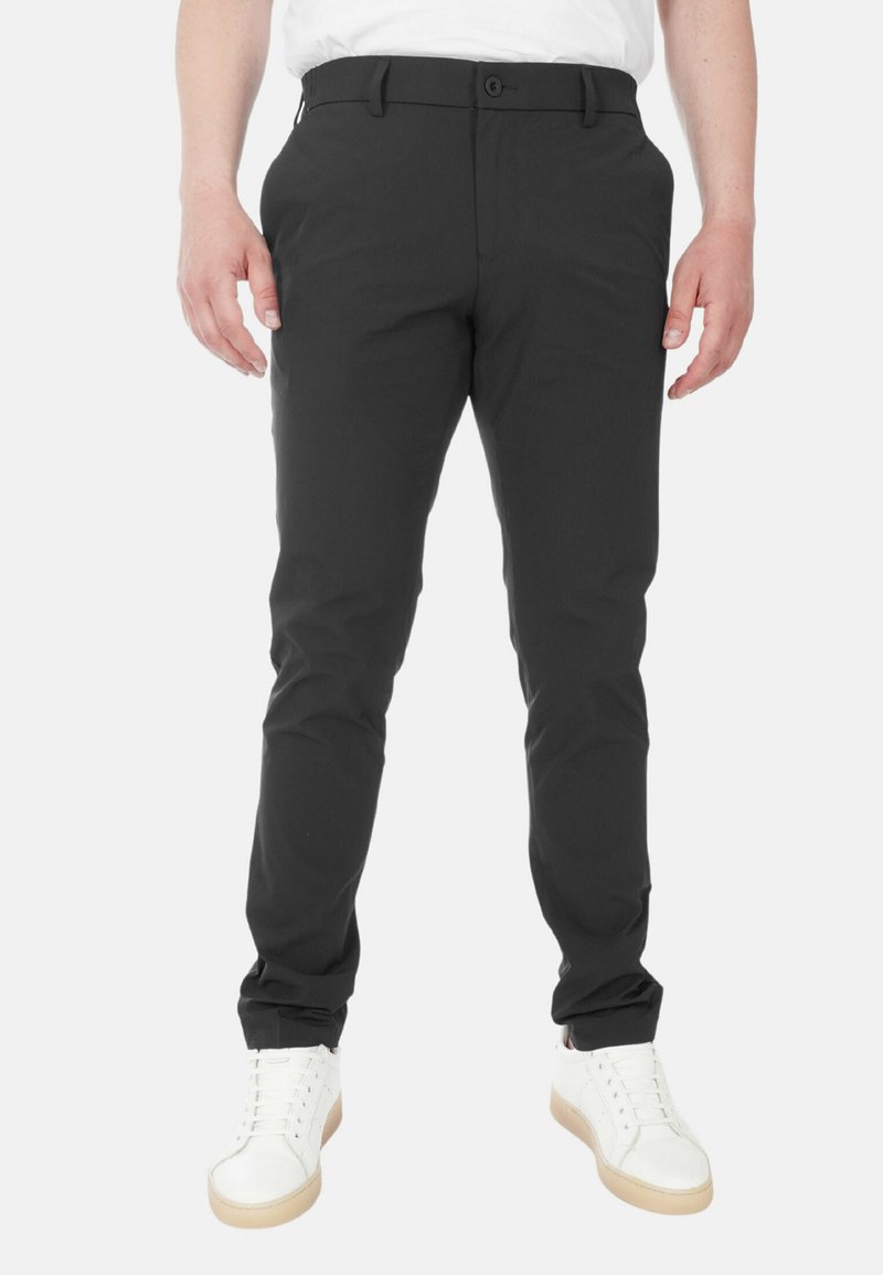 Pantaloni neri realizzati in un materiale liscio e elastico con una vestibilità affusolata, dotati di chiusura con bottone e passanti per cintura. Abbinati a sneaker bianche.