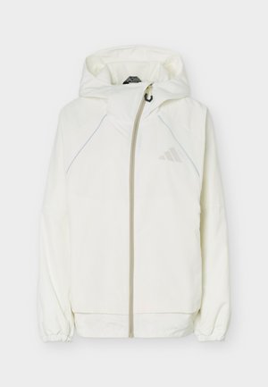 Veste blanche à capuche avec fermeture éclair sur le devant, poignets élastiques et logo Adidas discret sur la poitrine, présentée sur un fond uni.