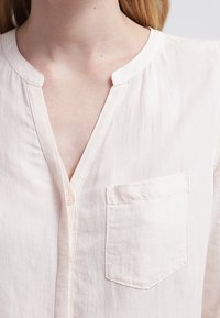 Camicia button-up rosa chiaro con scollatura a V, taschino sul petto e tessuto morbido e testurizzato. Design semplice con una vestibilità rilassata.
