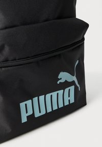 Μαύρο σακίδιο κατασκευασμένο από ανθεκτικό υλικό, με μεγάλο μπλε λογότυπο «PUMA» και γραφικό με ένα άλμα γάτας στο μπροστινό μέρος. Ορατό διαμέρισμα με φερμουάρ.