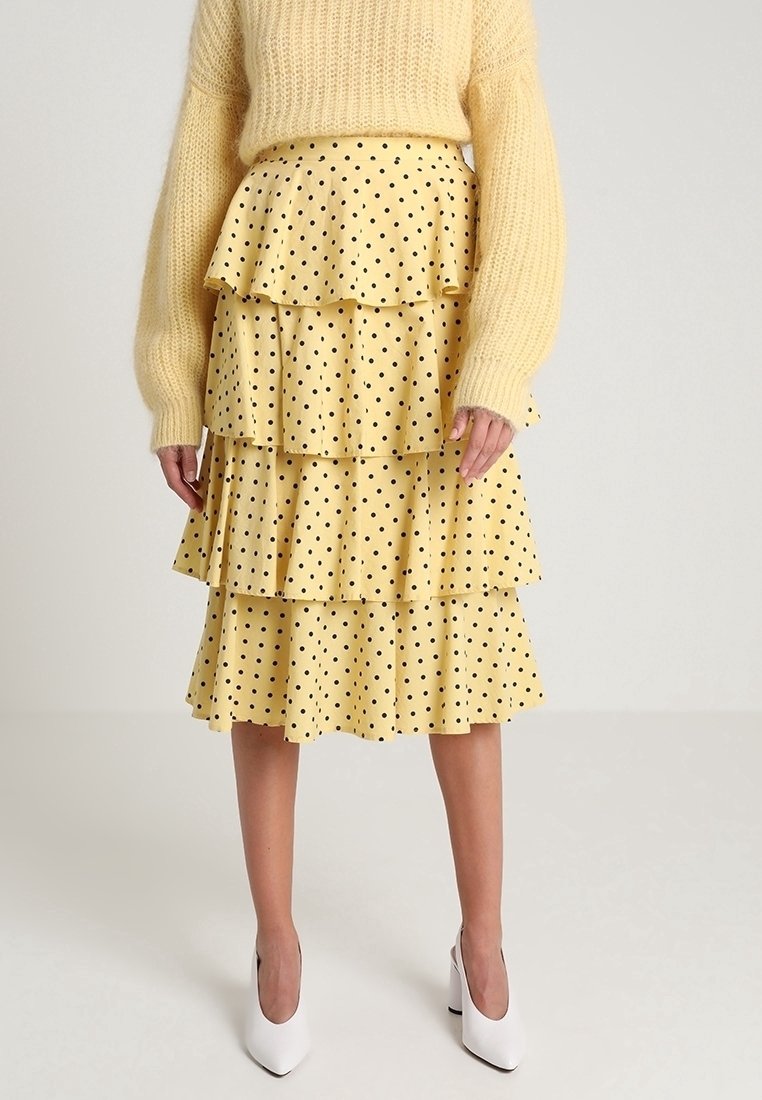 Gonna gialla a piani con pois neri abbinata a un maglione morbido giallo pallido e scarpe con tacco bianche.