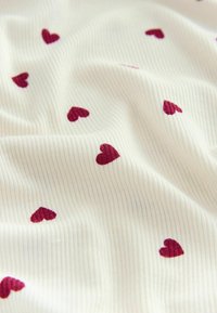 Cream fabric with a ribbed texture, featuring small burgundy hearts scattered throughout the surface.